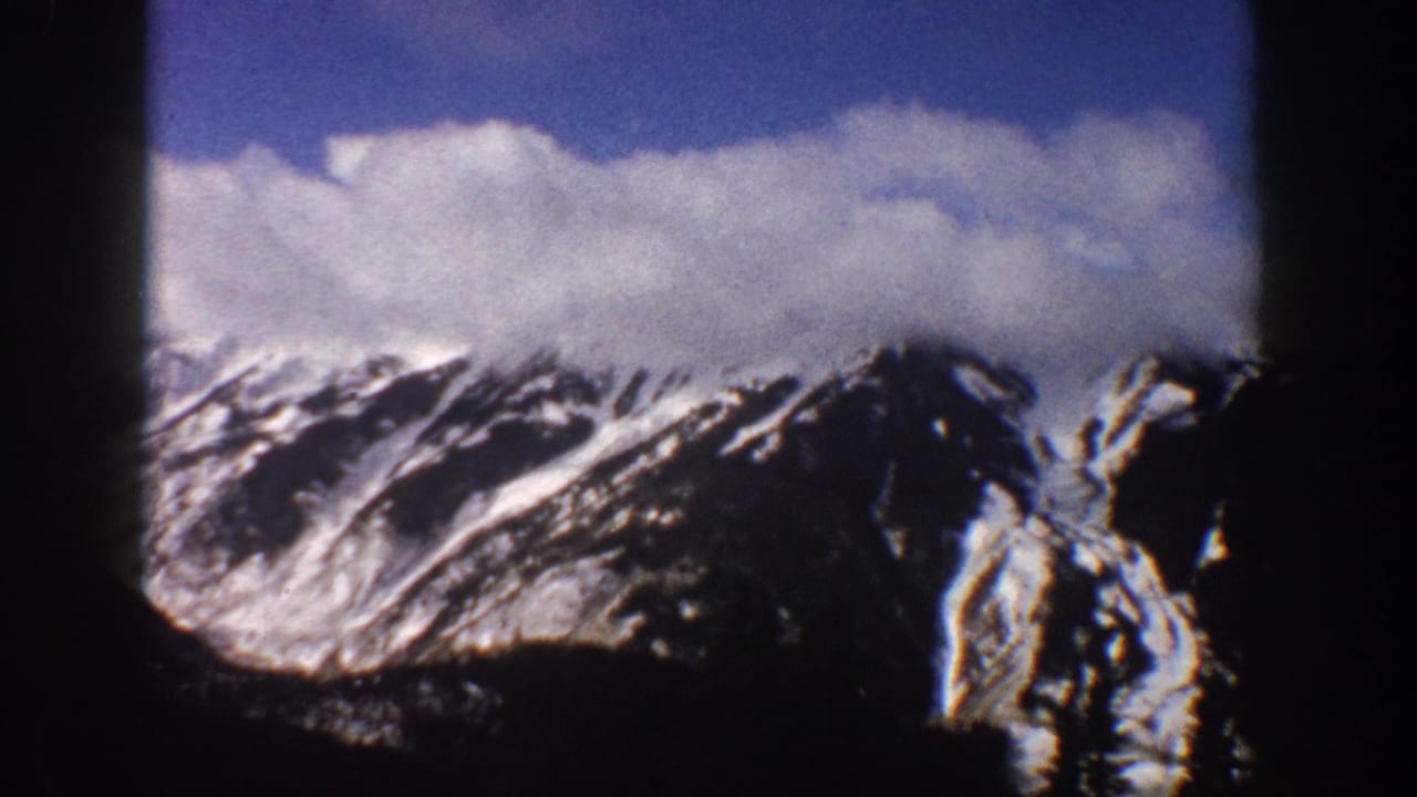 Snow-streaked mountain ridges under a partly cloudy sky, 8mm home movie.