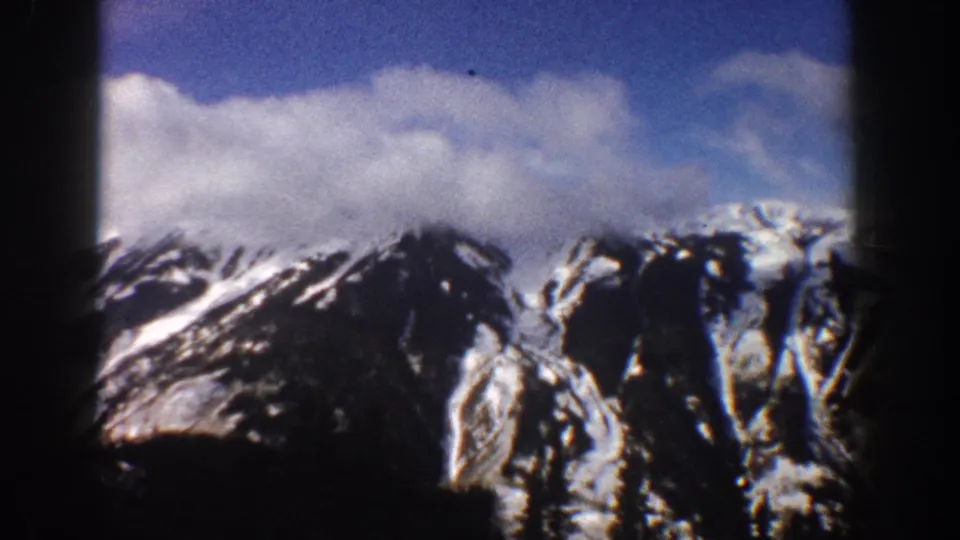 Lower slopes of Colorado Rocky Mountains with snow and dark conifer tips at frame base, filmed on 8mm circa 1961.