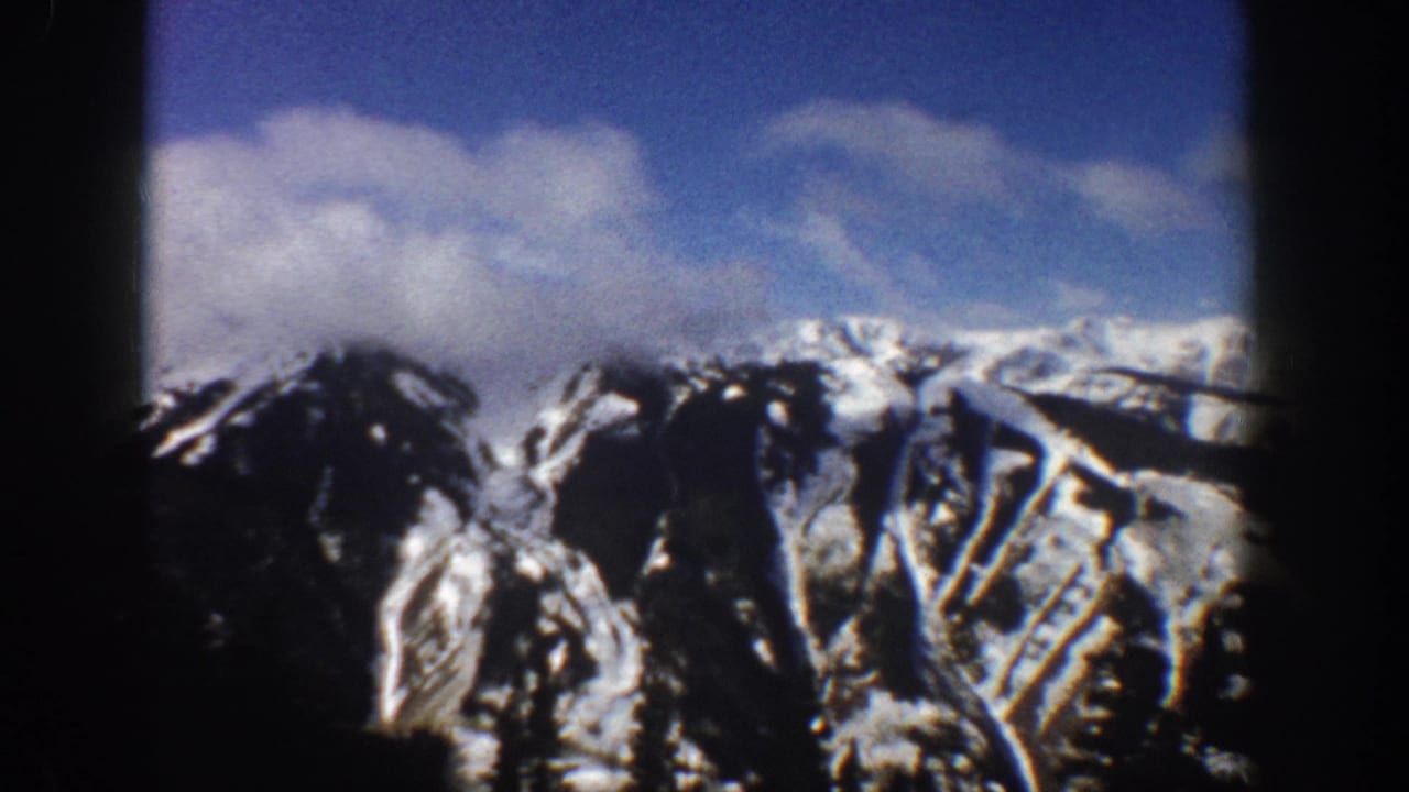 8mm home movie frame of a snow-covered mountain face in Aspen, Colorado, 1961, with blue sky and what appear to be ski-run clearings on the slopes.