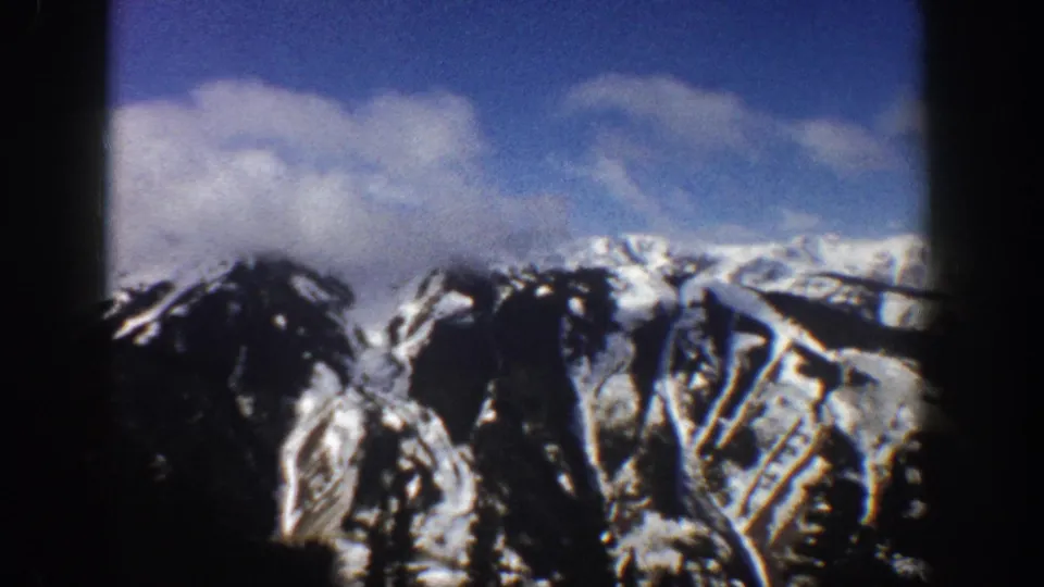 8mm home movie frame of a snow-covered mountain face in Aspen, Colorado, 1961, with blue sky and what appear to be ski-run clearings on the slopes.