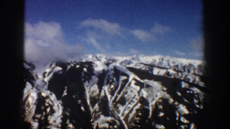 8mm frame showing snow-filled gullies and rocky upper slopes of a mountain in the Aspen, Colorado area, circa 1961, with blue sky above.
