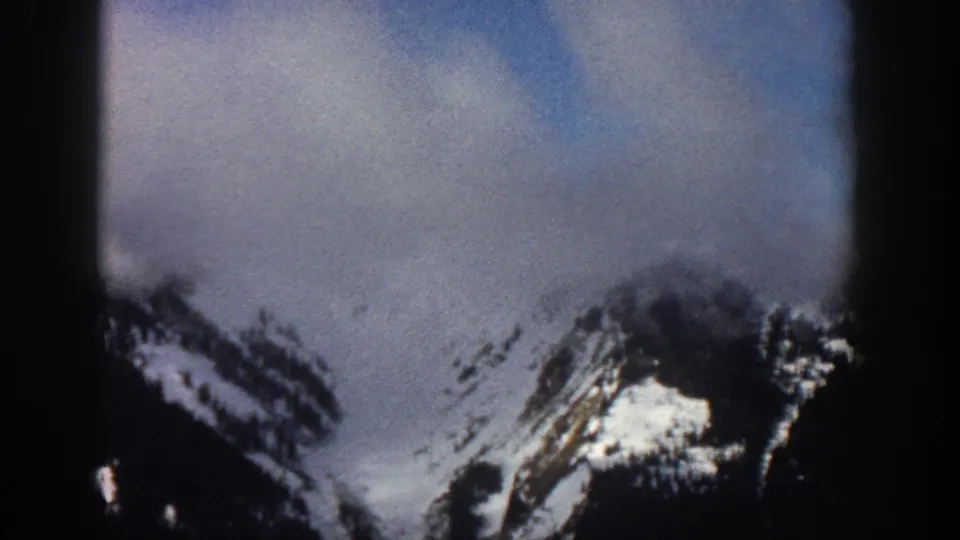 Similar mountain vista to frame 0, possibly Aspen, Colorado, circa 1961, with shifted cloud cover and visible 8mm grain.