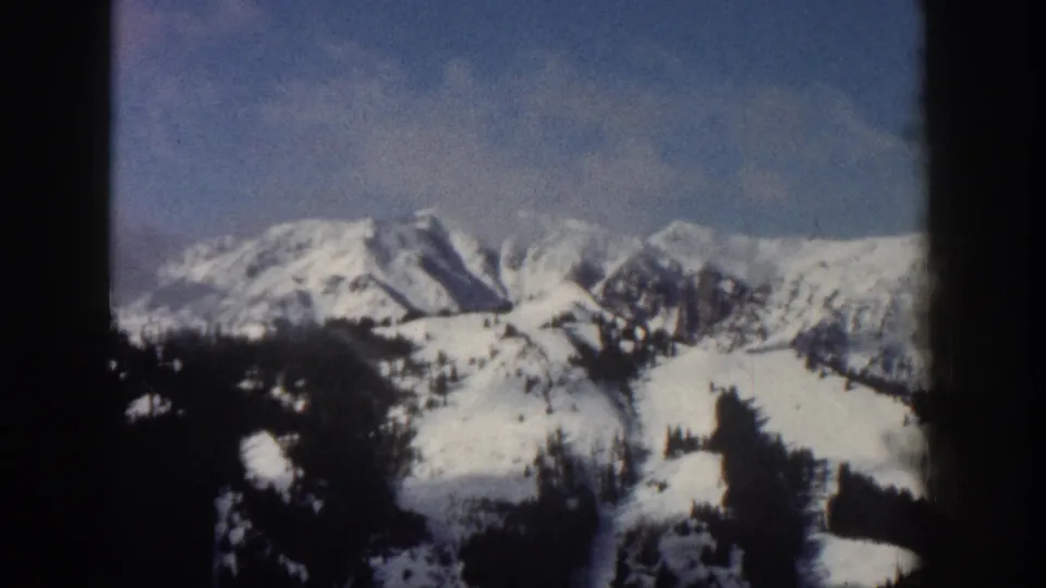 8mm frame from Aspen, Colorado, 1961, showing the snow-covered ridgeline with slightly shifted framing revealing more of the rocky peaks.