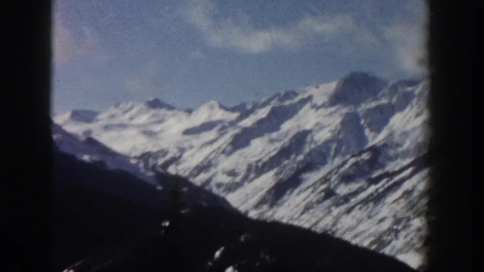 Final 8mm frame from Aspen, Colorado, 1961, revealing a wider open ridgeline with prominent snow-covered rocky peaks and a dark foreground slope.