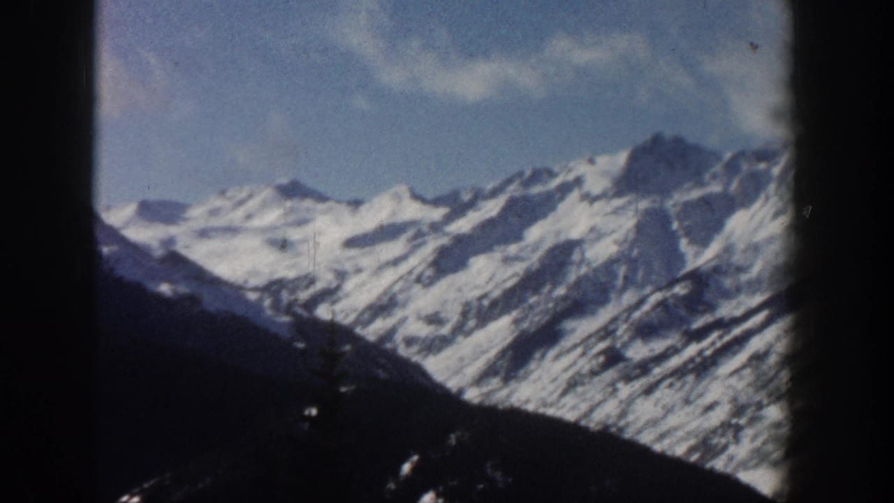 1961 8mm home-movie shot of snow-capped Rocky Mountain peaks near Aspen, Colorado, framed by a dark window edge at left.