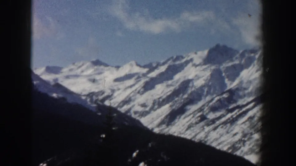 1961 8mm home-movie shot of snow-capped Rocky Mountain peaks near Aspen, Colorado, framed by a dark window edge at left.