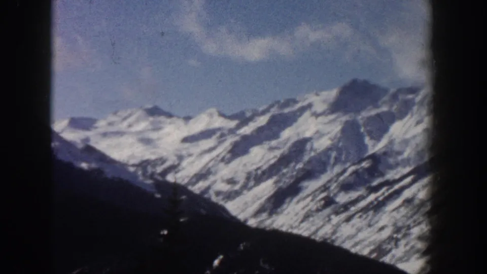 8mm home-movie frame from 1961 showing Aspen-area mountain ridgeline under partly cloudy blue sky, with dark vignette edges.