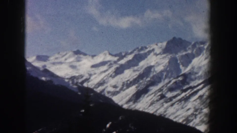 8mm home-movie frame from 1961 showing snow-covered alpine peaks near Aspen, Colorado, with dark conifer slopes in the foreground.