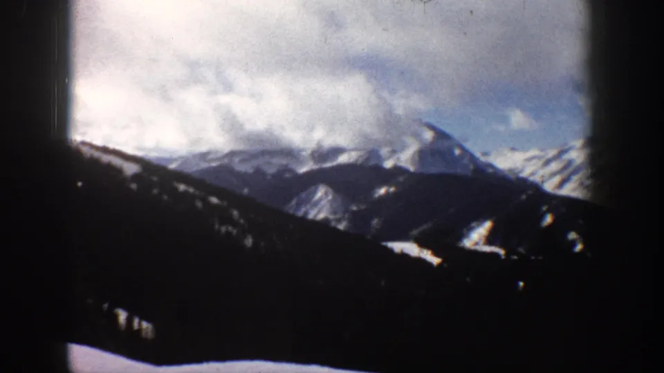 8mm landscape of snow-blanketed Rocky Mountain peaks near Aspen, Colorado, circa 1961, sky-heavy composition with dark foreground vignette from window framing.