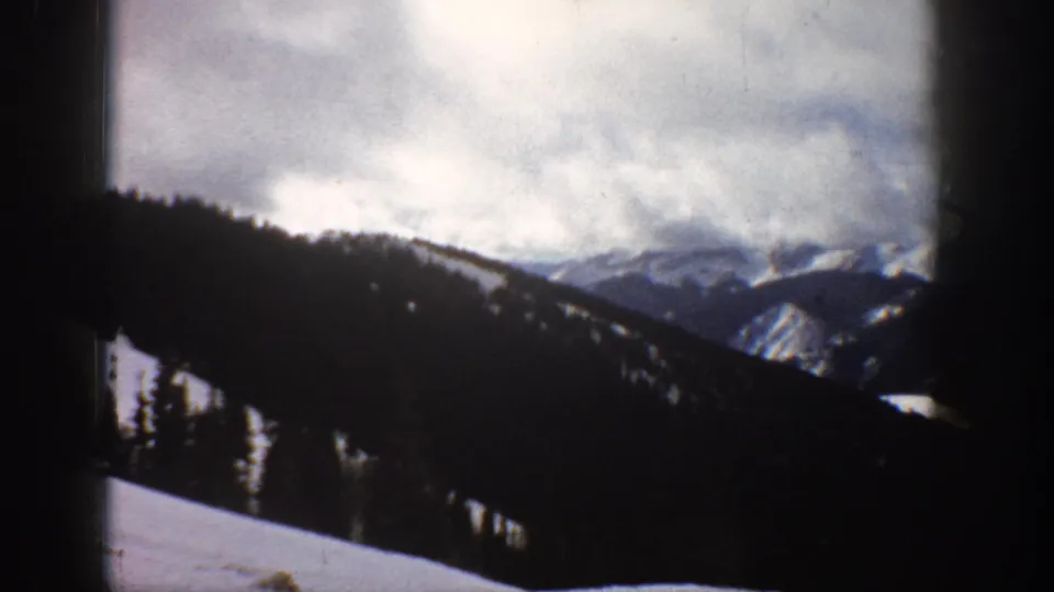 Alpine winter landscape circa 1961, camera shifted to reveal denser conifer treeline and snow-covered slope in foreground, Aspen area Colorado