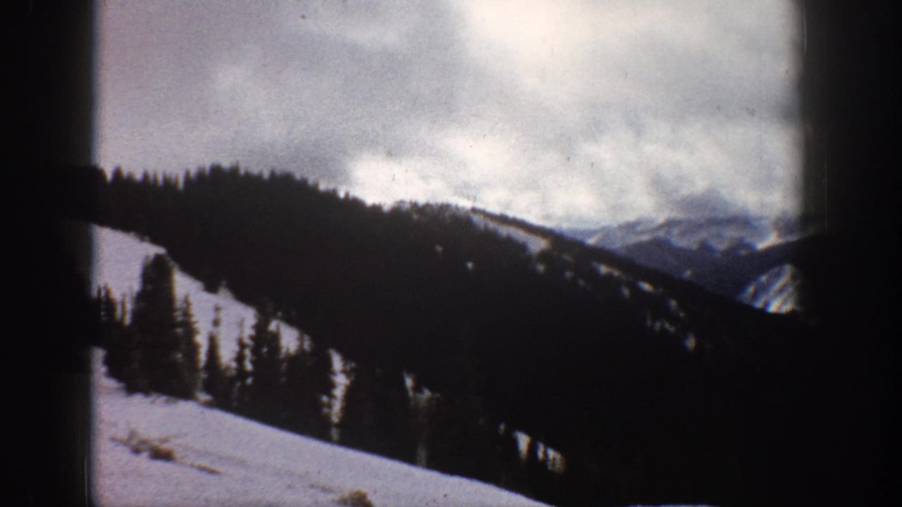 8mm home movie frame, Aspen Colorado area, 1961 — steep snow-covered forested mountain slopes beneath heavy cloud cover.