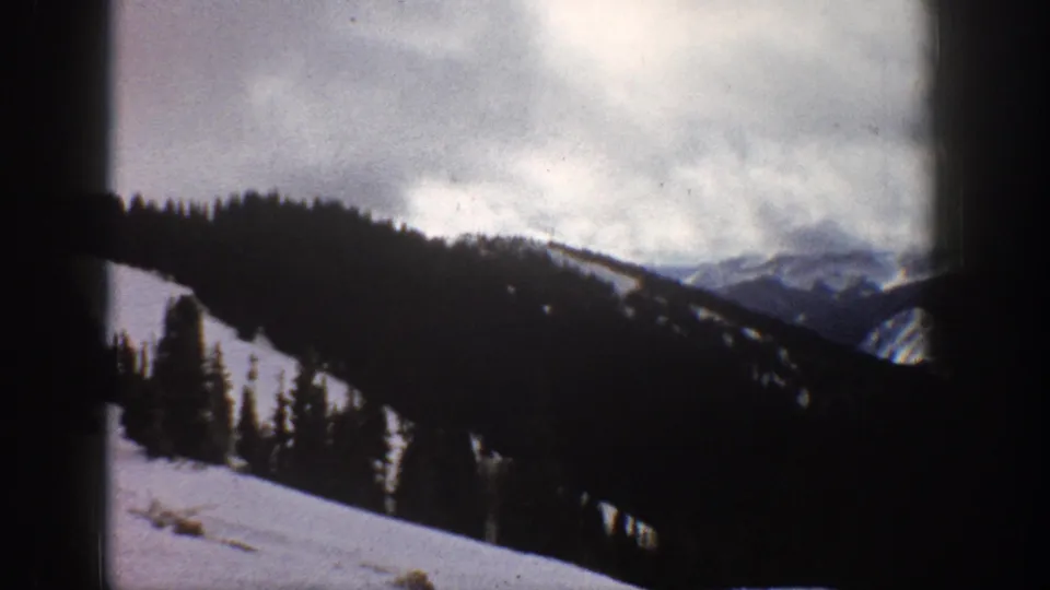 8mm home movie frame, Aspen Colorado area, 1961 — steep snow-covered forested mountain slopes beneath heavy cloud cover.