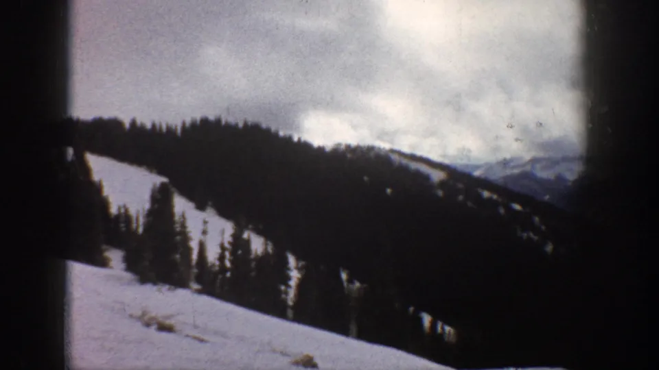 8mm home movie frame, Aspen Colorado area, 1961 — similar mountain vista with forested slopes and thick cloud cover obscuring distant peaks.