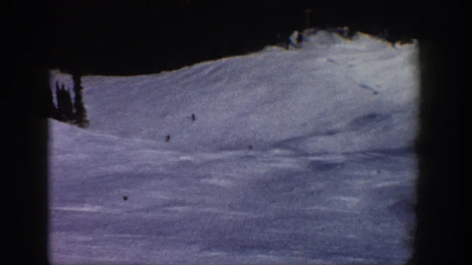 Final frame of 1961 8mm Aspen ski footage showing predominantly snow slope with treeline; cooler shadow tones and a possible lone skier visible in lower area.