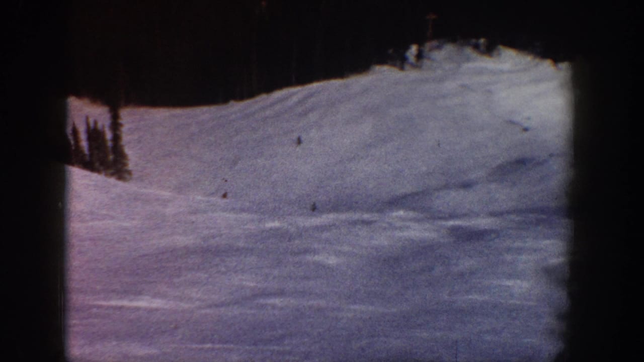 Wide ski slope view, likely Aspen, Colorado, circa 1961; 8mm color shift gives snow a blue-purple cast; tiny distant skiers visible; evergreen trees at ridge.