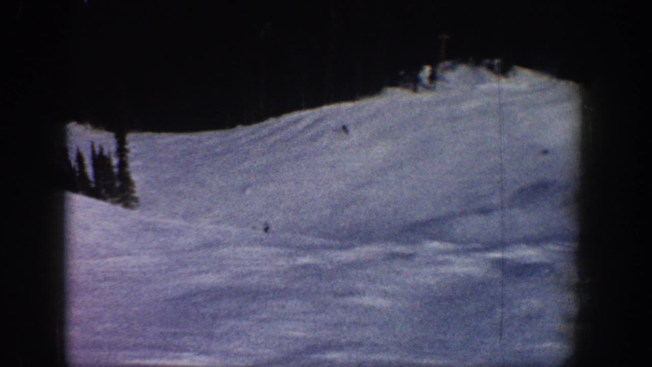 Wide ski run view consistent with a Colorado mountain resort, circa 1961; 8mm reversal stock shows blue-purple snow tone and grain; distant skiers appear as small specks.