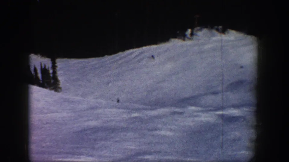 Wide ski run view consistent with a Colorado mountain resort, circa 1961; 8mm reversal stock shows blue-purple snow tone and grain; distant skiers appear as small specks.