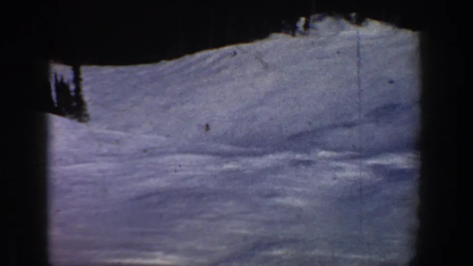 Wide ski run view, likely same Colorado mountain location, circa 1961; a vertical film scratch bisects the frame — a physical artifact on the 8mm original.
