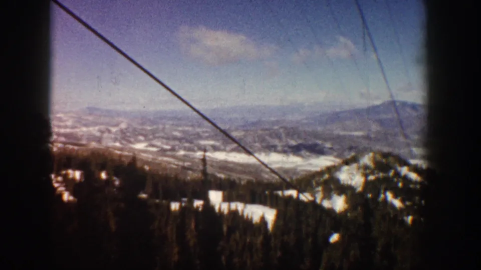 Moving 8mm shot from a ski lift at Aspen, Colorado, circa 1961, showing a snow-covered mountain peak, evergreen forest slopes, and a broad alpine valley.