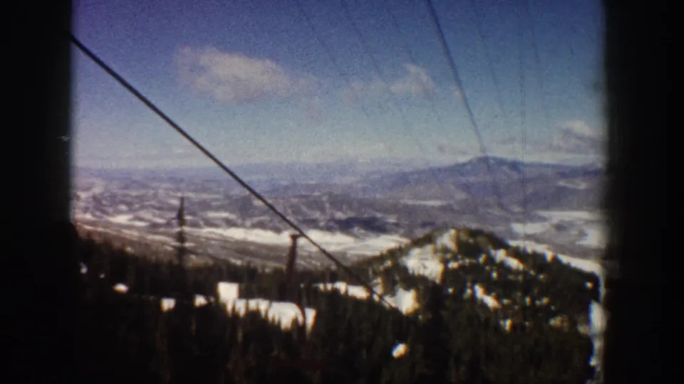 8mm ski lift footage over Aspen, Colorado, circa 1961, showing snowy slopes, conifer forest, and a distant valley that may include early resort-era development.