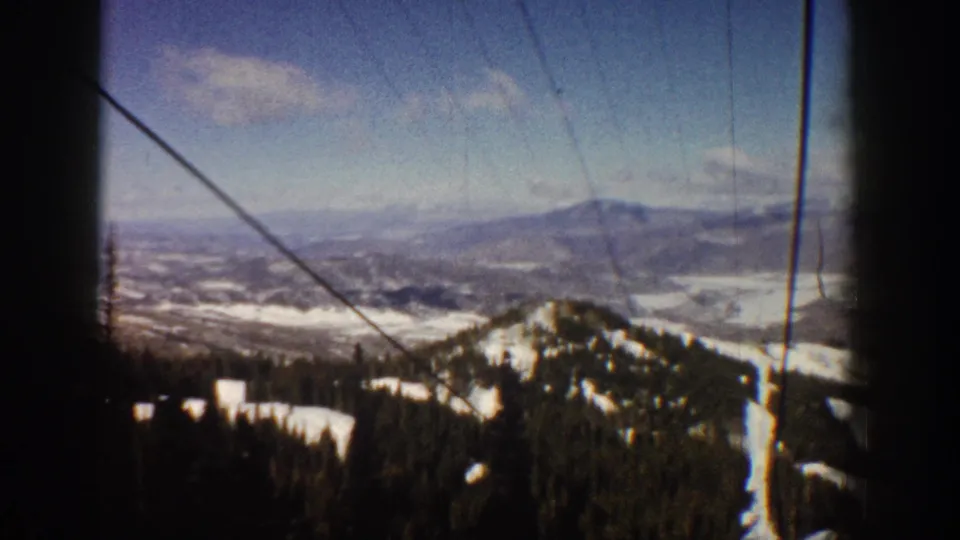 Final frame of 8mm ski lift sequence at Aspen, Colorado, circa 1961, showing a prominent snow-covered peak, evergreen slopes, and a wide alpine valley.