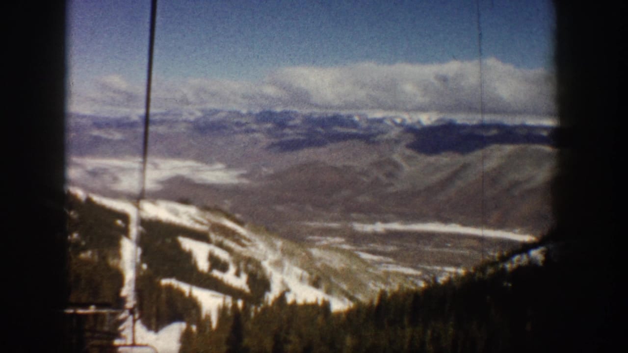 8mm home-movie panorama shot from ski-lift height looking across a broad Colorado mountain valley with conifer treeline below, circa 1961.