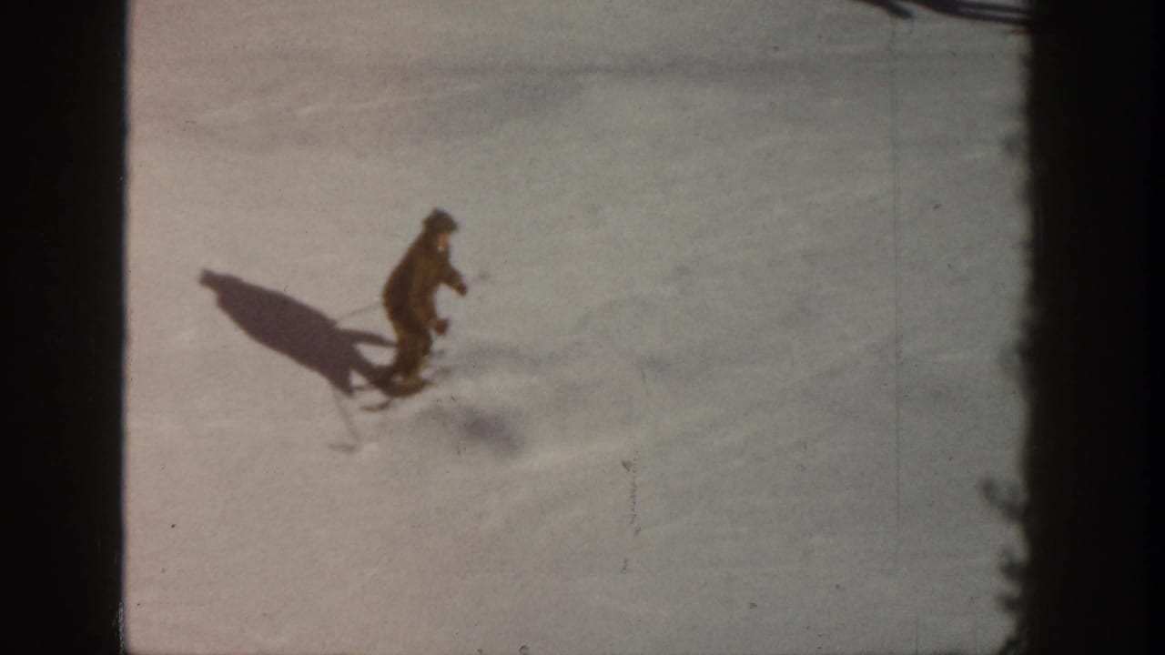 One skier in dark winter clothing descends a sunlit snow slope in what is identified as Aspen, Colorado, circa 1961, captured on 8mm film.