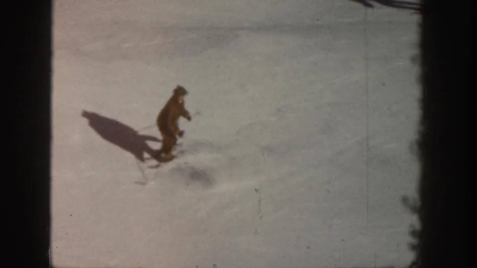 One skier in dark winter clothing descends a sunlit snow slope in what is identified as Aspen, Colorado, circa 1961, captured on 8mm film.