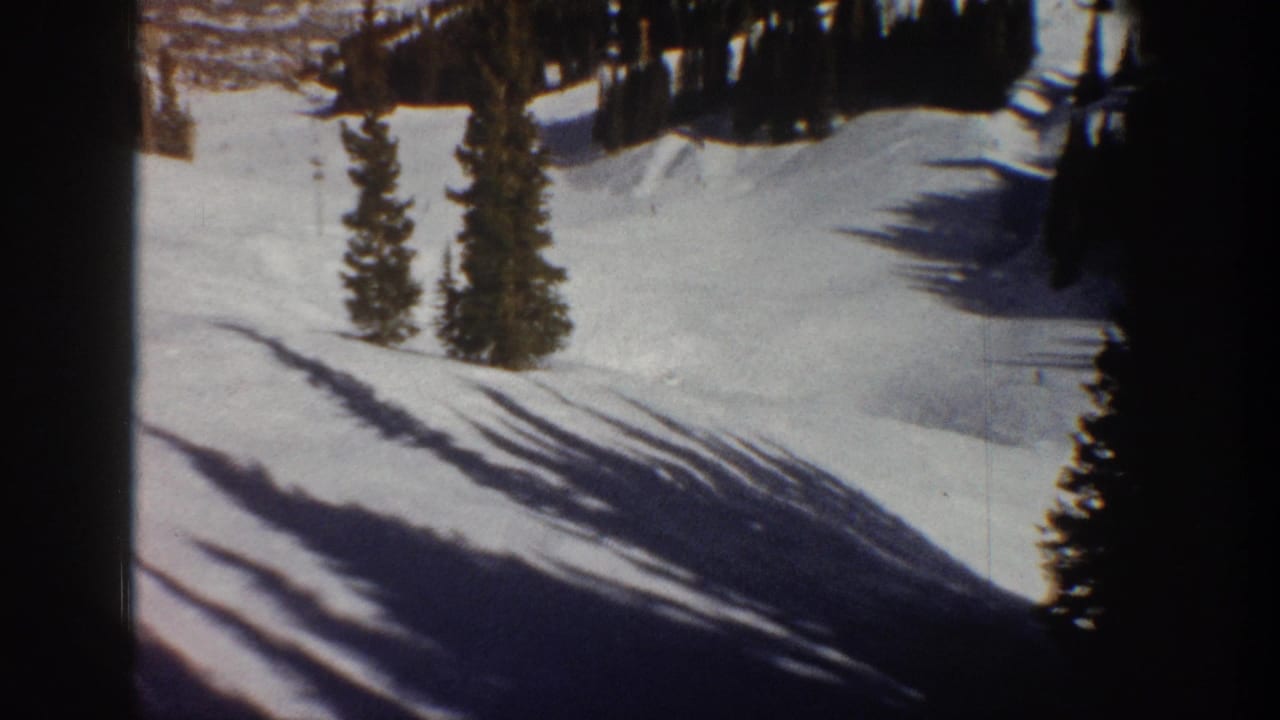 8mm film frame showing a snow-covered Rocky Mountain slope with evergreen pines and long winter shadows, Aspen Colorado area, circa 1961.