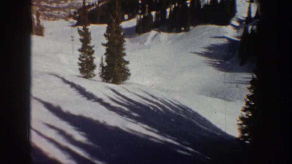 8mm film frame showing a snow-covered Rocky Mountain slope with evergreen pines and long winter shadows, Aspen Colorado area, circa 1961.
