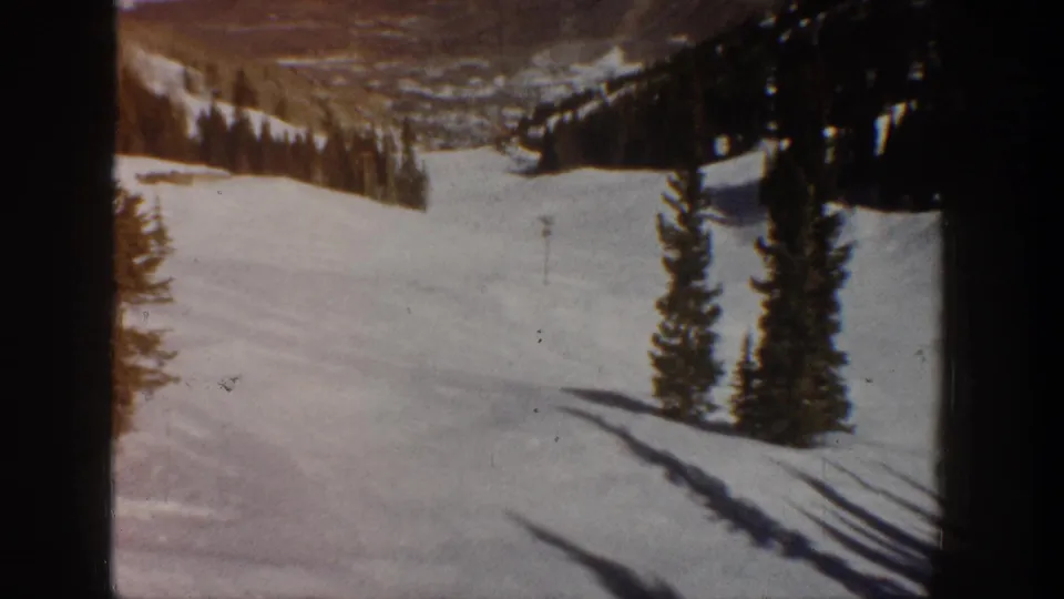 8mm color film frame at the end of a pan showing a snow-covered slope, pine trees, and a distant valley below, Aspen Colorado area, circa 1961.