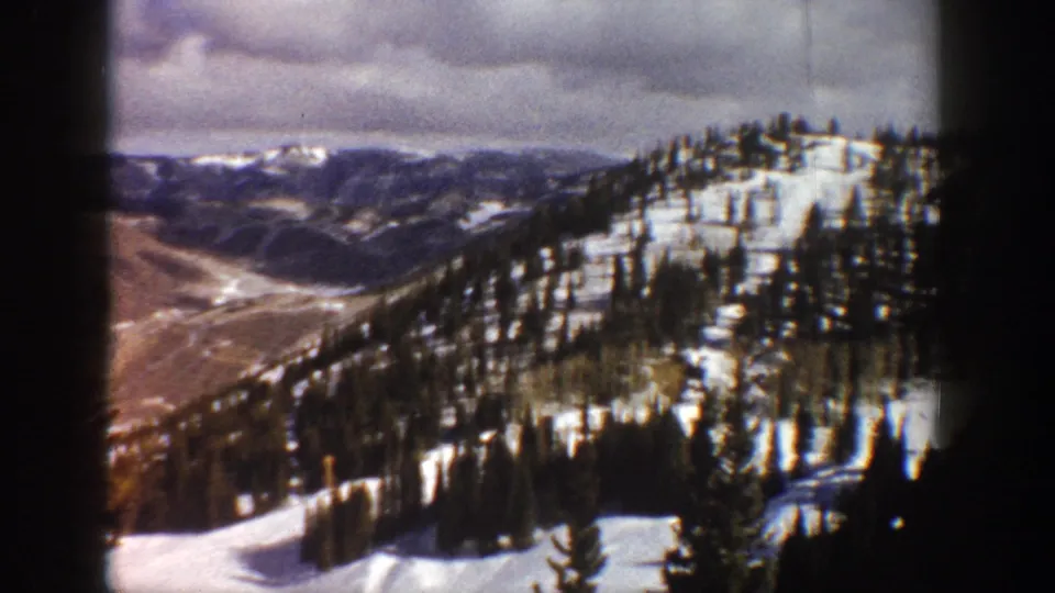 8mm home-movie frame showing a mountain valley corridor between snow-covered conifer slopes, Aspen area, Colorado, ca. 1961.