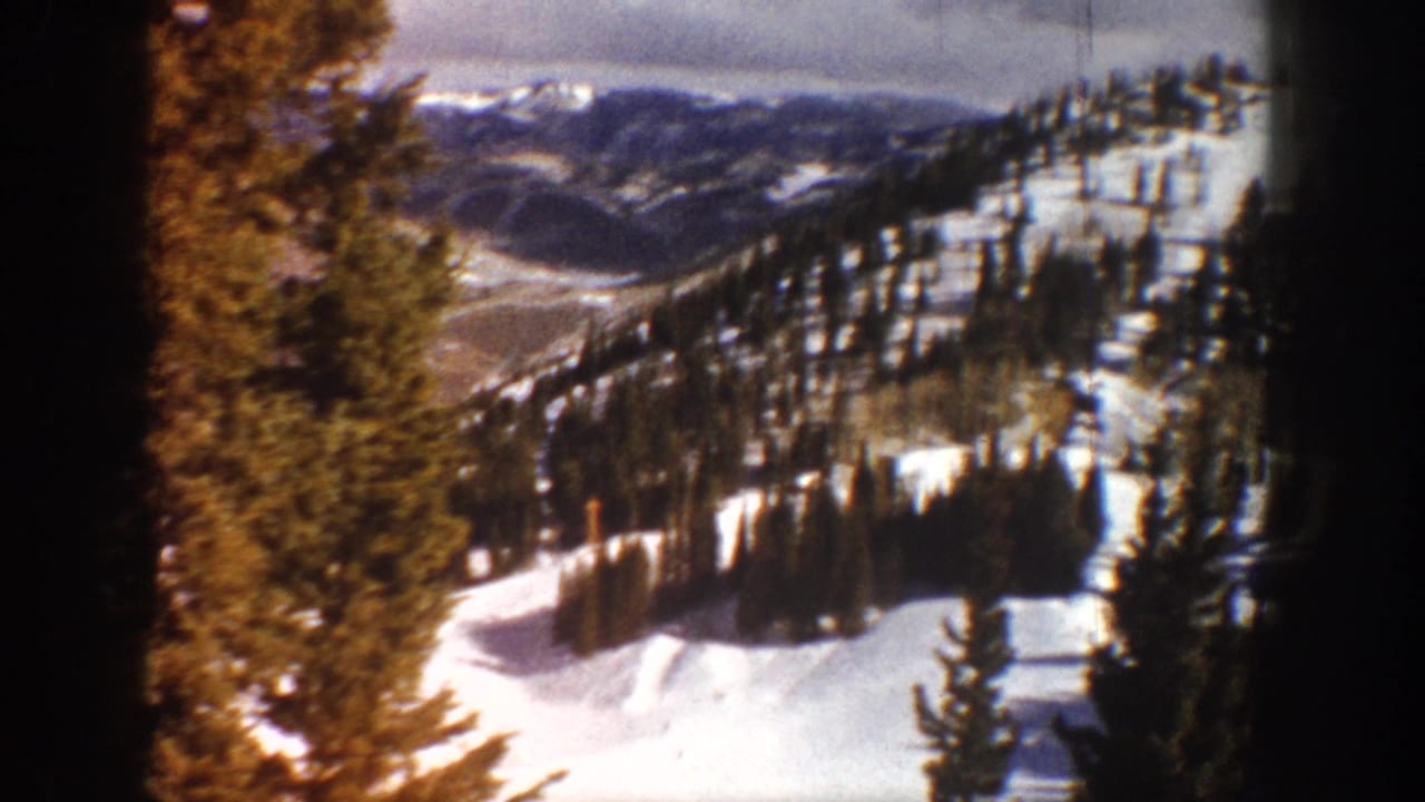 Snow-covered Colorado mountain valley with evergreen-forested slopes under grey clouds, circa 1961, 8mm home movie footage.