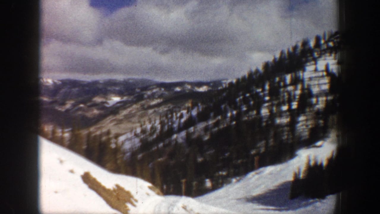 Panoramic view of snow-covered Colorado mountain ridgelines with dense conifer forest under overcast sky, circa 1961, 8mm home movie.