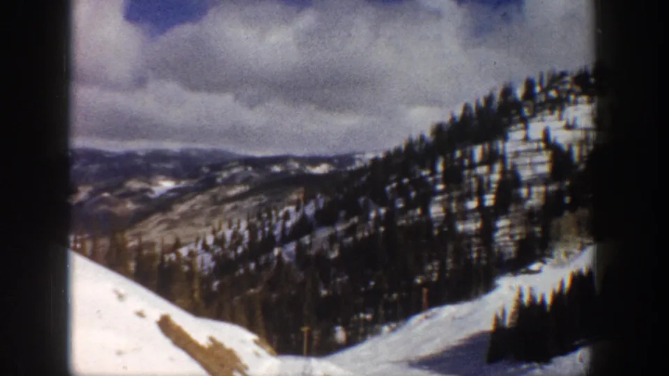 Wide alpine slope and evergreen-covered ridgelines under overcast sky in Colorado mountains, circa 1961, 8mm home movie footage.