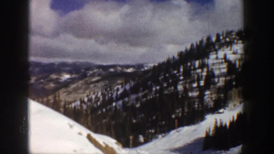 Continuing pan across snow-covered Colorado mountain valley with conifer forest and overcast winter sky, circa 1961, 8mm home movie.