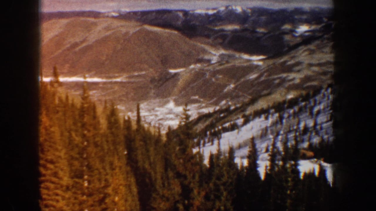 1961 Aspen, Colorado 8mm view of snow patches, evergreen pines, and brown mountain slopes framed by a dark vertical edge.