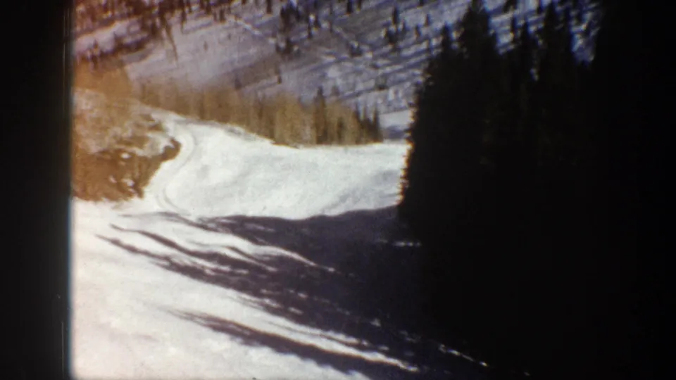 Winding snowy road or track below pine-covered slopes near Aspen, Colorado, seen in soft 8mm home-movie footage.