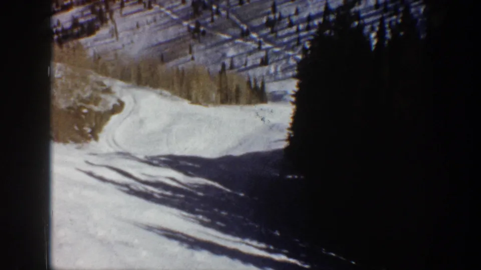 1961 Aspen home-movie frame showing a winding snowy road beside dense evergreens and hillside shadows.