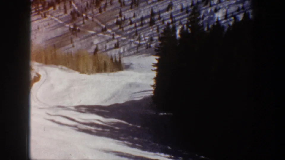 Metadata-supported 1961 Aspen footage showing a snowy road below evergreens with long shadows across the surface.