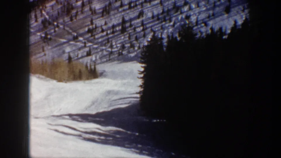1961 Aspen 8mm frame showing a snow-covered slope bordered by dark evergreen trees, with soft focus and visible film edges.