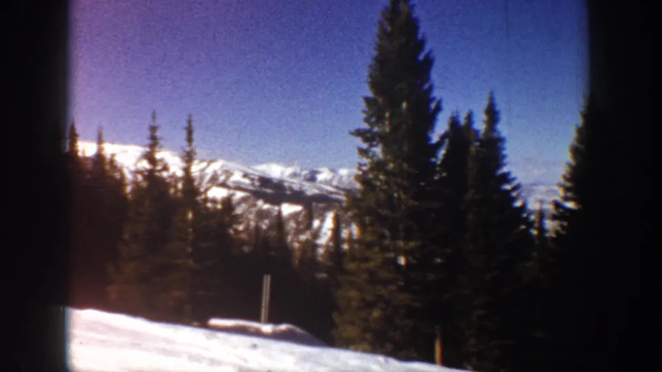 1961 Aspen 8mm frame with dark conifers, bright snow in the foreground, and distant white mountain ridges under blue sky.