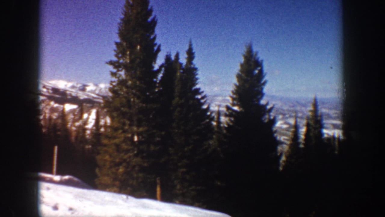 1961 Aspen, Colorado home-movie frame showing evergreen trees, snow, distant ridges, and dark window divisions.