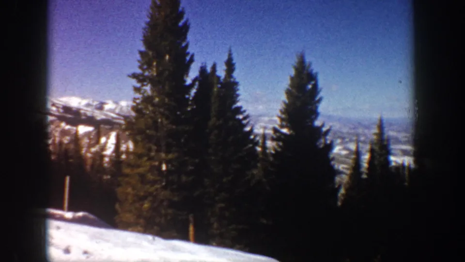 1961 Aspen, Colorado home-movie frame showing evergreen trees, snow, distant ridges, and dark window divisions.