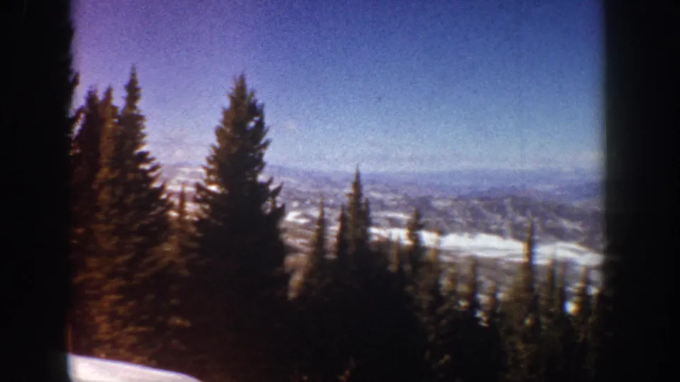 1961 Aspen, Colorado frame with a dark window edge, conifers, snow-covered ground, and layered mountain ridges beyond.