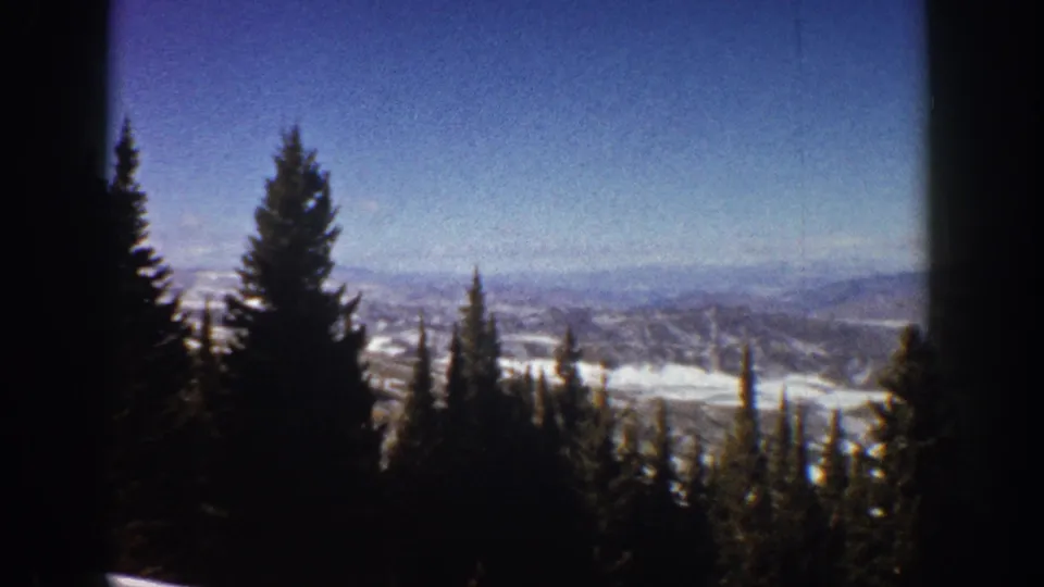 1961 Aspen, Colorado home-movie still showing a window-framed winter landscape with evergreens and distant snowy slopes.
