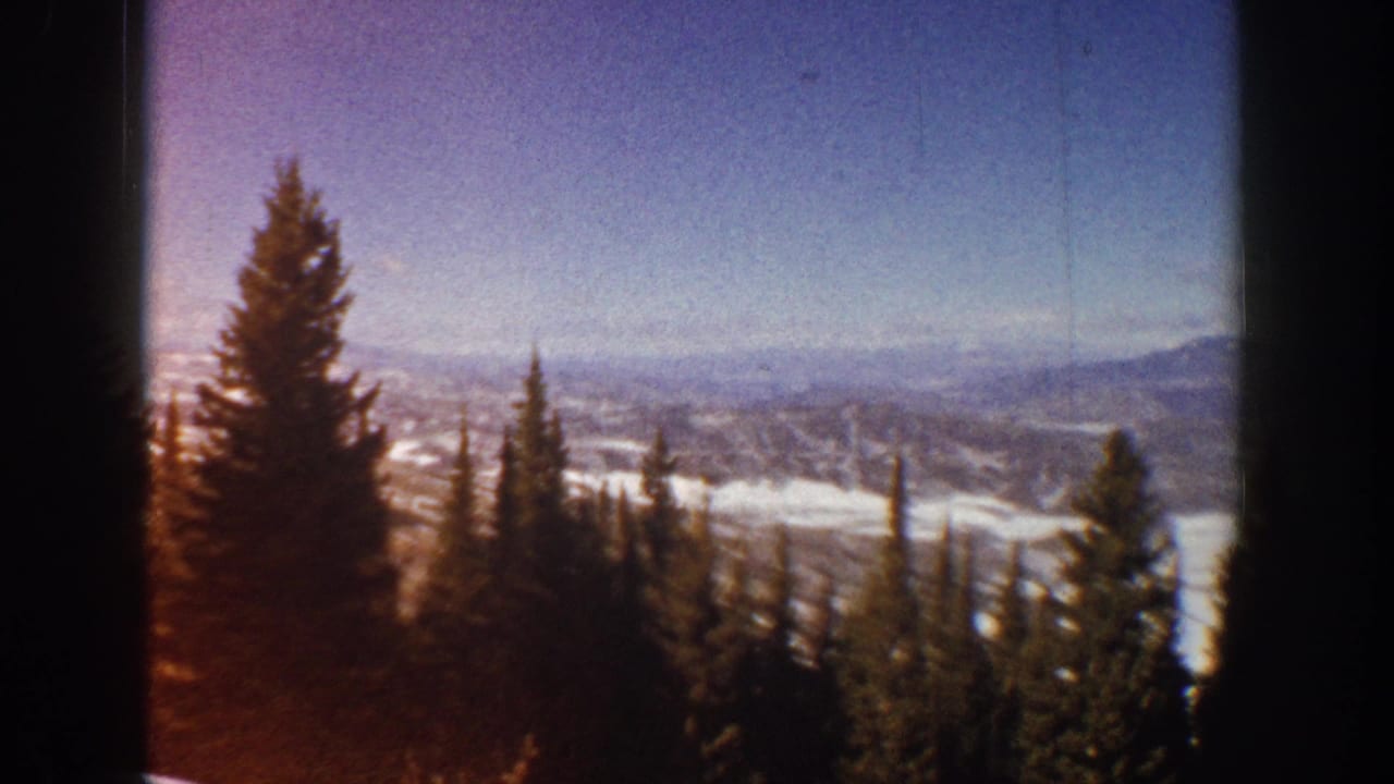 1961 Aspen-area 8mm view of pine trees, snow-dappled ridges, and a blue sky seen through dark window or film-frame borders.