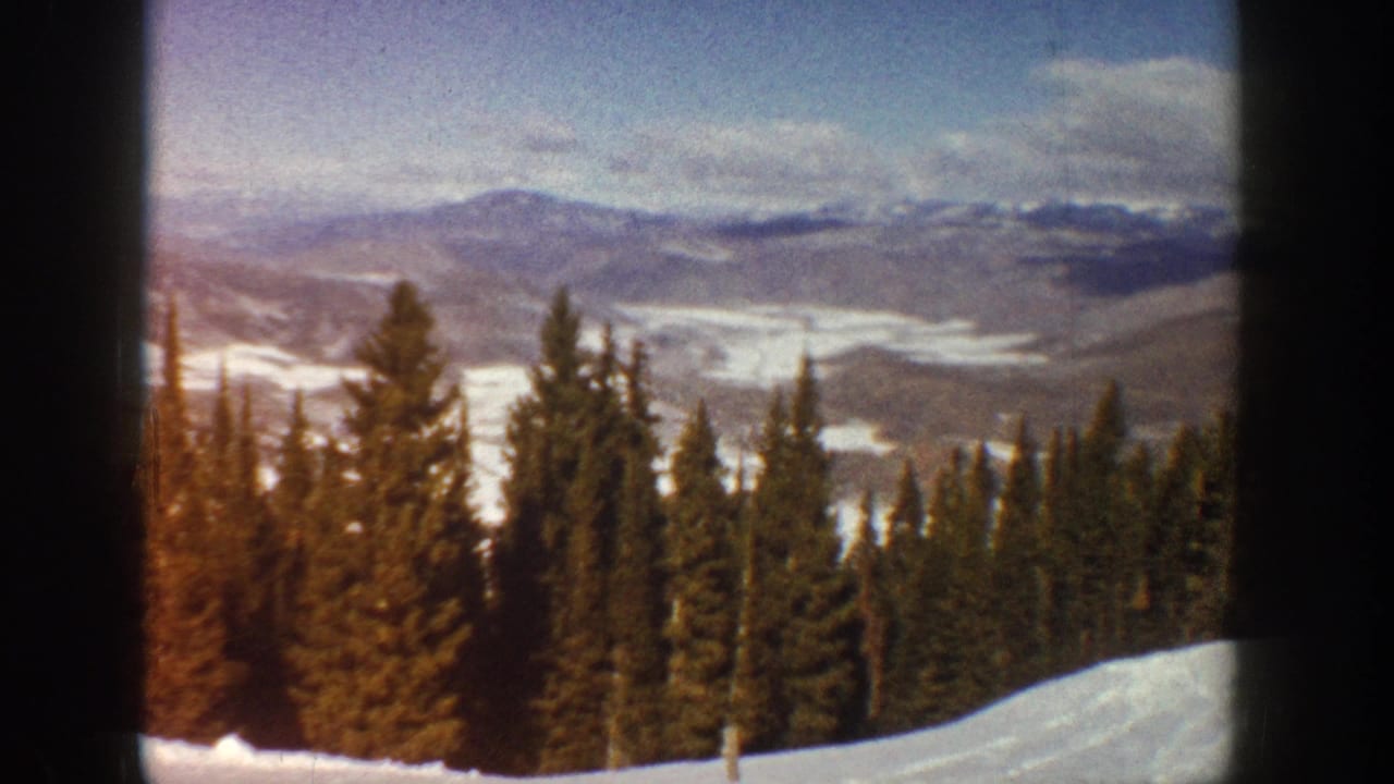 1961 Aspen-area 8mm frame showing a snowy slope, dark evergreens, and distant Colorado mountain ridges.