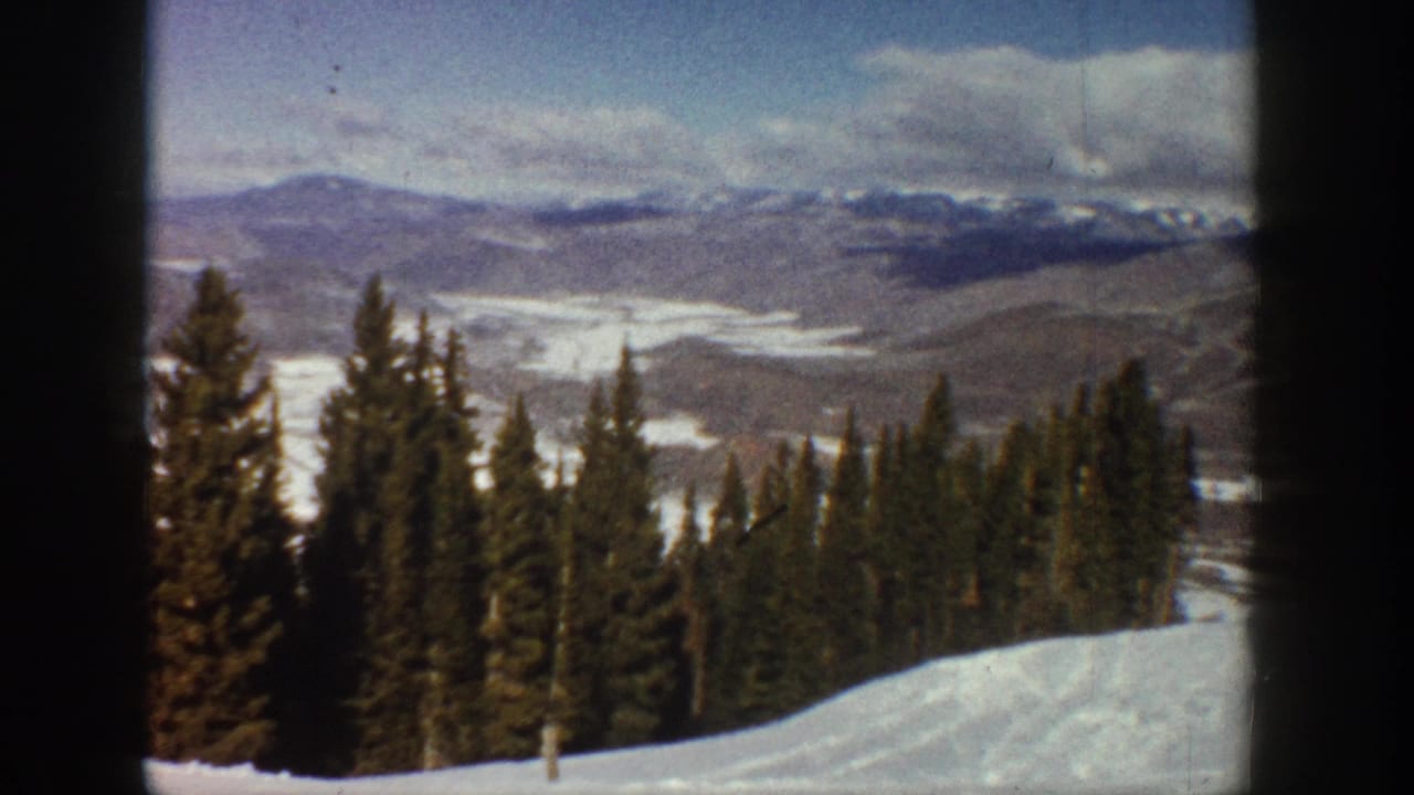 1961 Aspen-area 8mm frame with a snowy foreground, tall evergreens, distant ridges, and soft winter light.