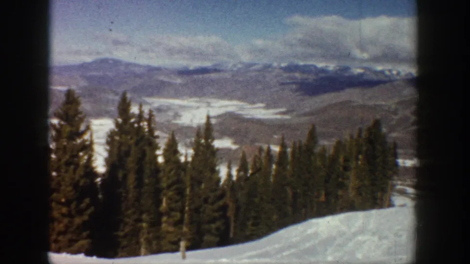 1961 Aspen-area 8mm frame with a snowy foreground, tall evergreens, distant ridges, and soft winter light.